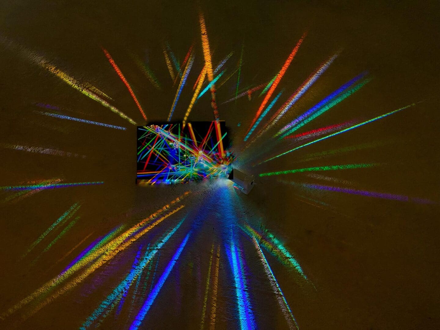 Abstract image with colorful light beams radiating from a central dark square.