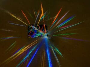 Colorful light rays radiate from a small central prism against a dark background.