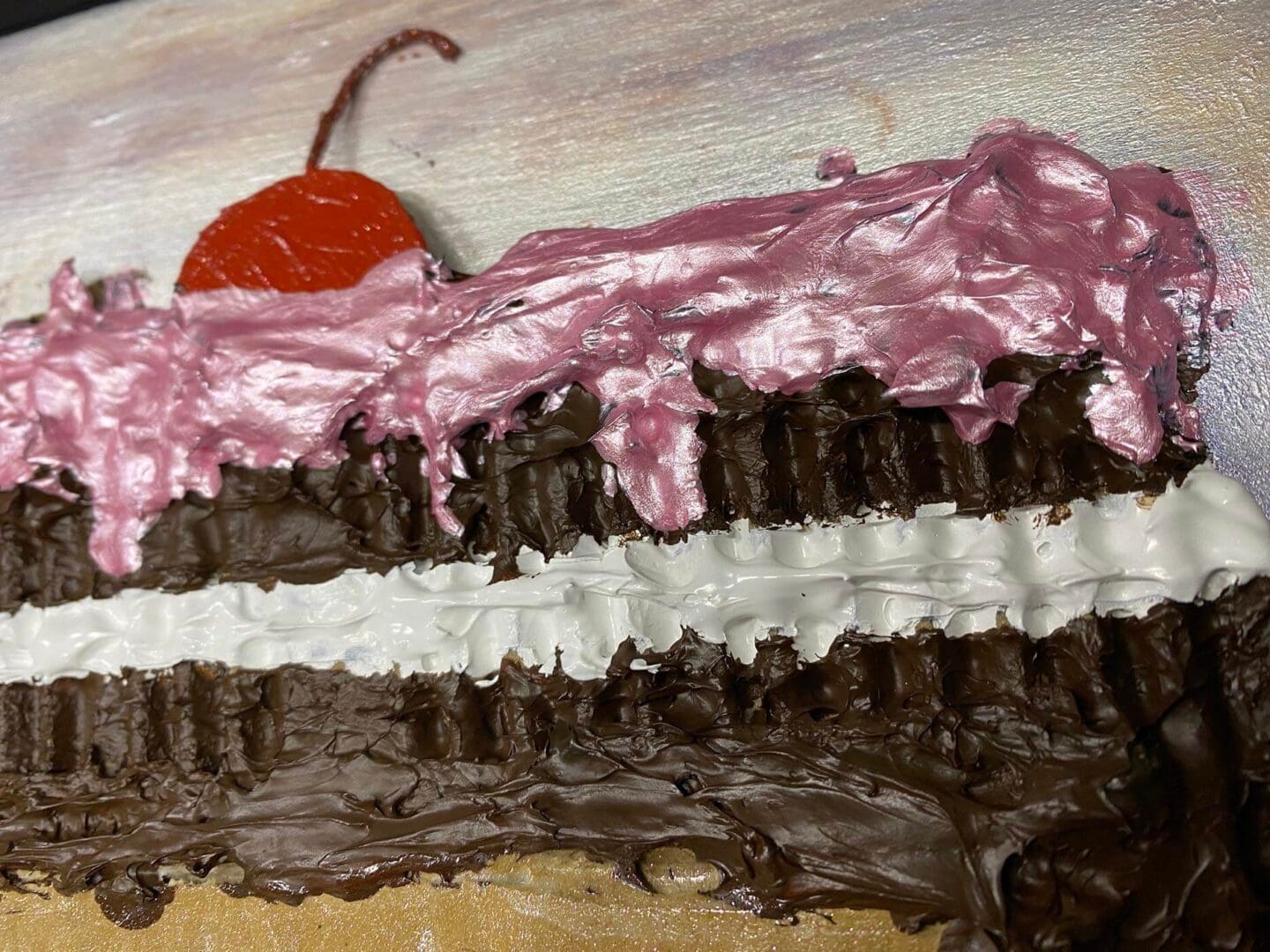 A slice of layered chocolate cake with pink frosting and a cherry on top.